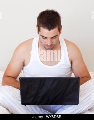Serious  man using a laptop in his bedroom Stock Photo