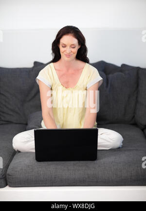 Happy woman using a laptop on a grey sofa Stock Photo