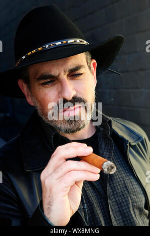 Man with beard in cowboy hat smoking cigar Stock Photo