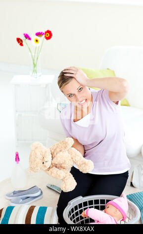 Blond young woman with headache putting toys into a basket in the living room Stock Photo