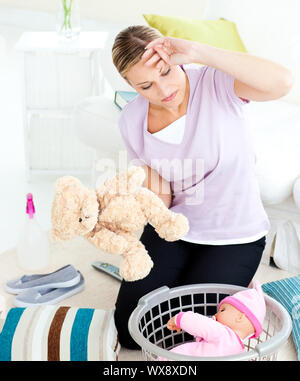 Exhausted young woman putting toys into a basket in the living room Stock Photo