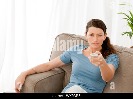 Charismatic woman watching television at home and changing channel Stock Photo
