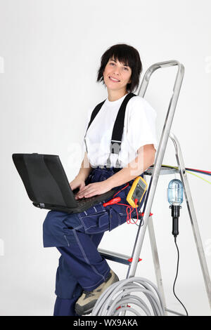 Female electrician sat on ladder with laptop Stock Photo
