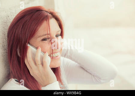 Pretty smiling redheaded woman against an old wall making a call with her cell phone Stock Photo