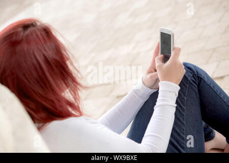 Pretty smiling redhead woman sending messages on her cell phone in a park. . Focus on her phone Stock Photo