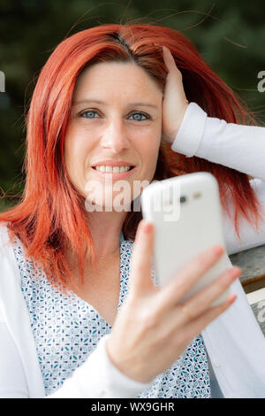 Portrait of smiling beautiful young woman close up with mobile phone, against background of summer green park. Stock Photo