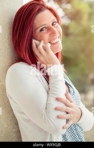 Pretty smiling redheaded woman against an old wall making a call with her cell phone Stock Photo