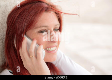 Pretty smiling redheaded woman against an old wall making a call with her cell phone Stock Photo