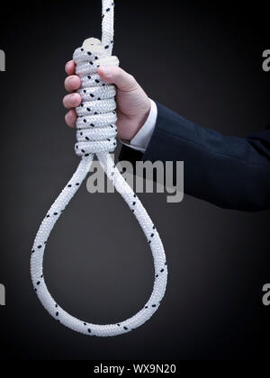 A man on a suit holds a hangman's noose over a gray background. Stock Photo