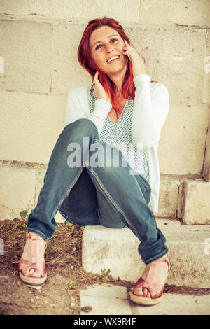 Pretty smiling redheaded woman against an old wall making a call with her cell phone Stock Photo