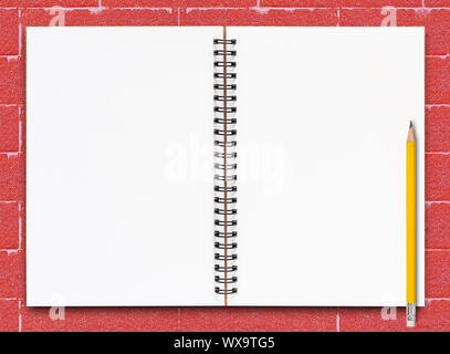 Open notebook and yellow pencil on red brick background Stock Photo