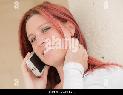 Pretty smiling redheaded woman against an old wall making a call with her cell phone Stock Photo