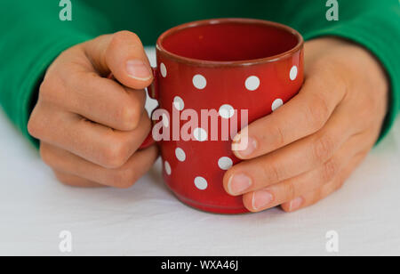 woman holding a red coffee cup with white polka dots on a white table cloth Stock Photo