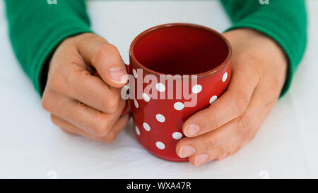 woman holding a red coffee cup with white polka dots on a white table cloth Stock Photo
