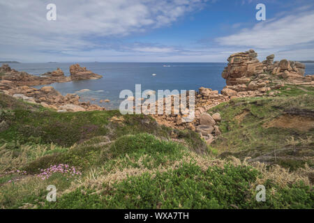 Overview of craggy rock formations framing a sunny cove along Brittany’s Pink Granit Coast, the Côte de granit rose, near Ploumanach, France. Stock Photo
