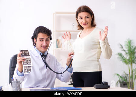 Old pregnant woman visiting young male doctor Stock Photo