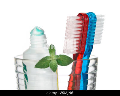 Toothbrushes, toothpaste and mint leaves in a glass over white background. Stock Photo