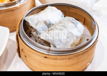 Delicious Lo Mai Gai dim sum, fresh steamed glutinous rice with chicken roll wrapped by lotus leaf in bamboo steamer in hong kong yumcha restaurant. Stock Photo