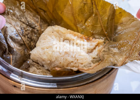 Delicious Lo Mai Gai dim sum, fresh steamed glutinous rice with chicken roll wrapped by lotus leaf in bamboo steamer in hong kong yumcha restaurant. Stock Photo