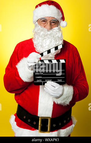 Its time for next shot. Cheerful Kris Kringle posing with clapperboard. Stock Photo