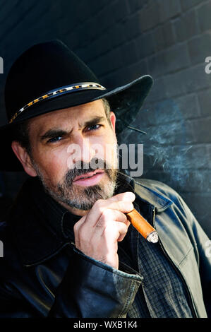 Man with beard in cowboy hat smoking cigar Stock Photo