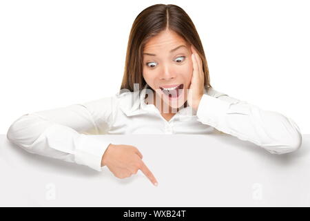 advertising banner sign - woman excited pointing looking down on empty blank billboard paper sign board. Young business woman isolated on white backgr Stock Photo