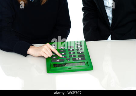 Cropped image of teacher and a student working out on a large green calculator. Stock Photo