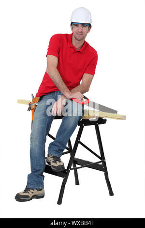 Man with a saw sitting on a workbench Stock Photo