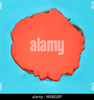 Burnt hole in turquoise paper with burned edges, flat lay on vibrant orange paper with copy-space Stock Photo