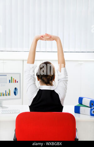 Rear view of young businesswoman sitting at desk stretching. Copy space Stock Photo