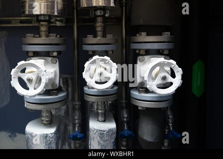 several bright white water mains valves with black and insulated pipes and close instructions in f Stock Photo