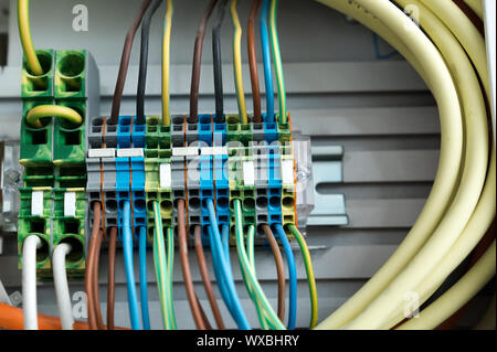 many colorful electrical wires lead into a relay and transformer panel on a wall Stock Photo
