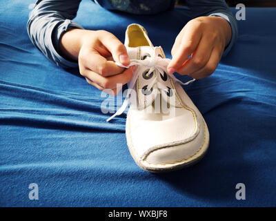 Boy is learning how to tie shoelaces, close-up on the hands and the shoe on blue textile background Stock Photo