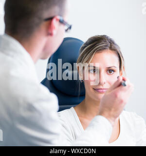 optometry concept - pretty young woman having her eyes examined by an eye doctor Stock Photo