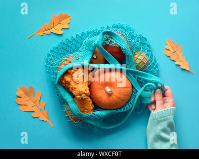 Autumn flat lay with female hand holding turquoise string bag with orange pumpkins.Top view on paper  background in on blue mint color. Stock Photo