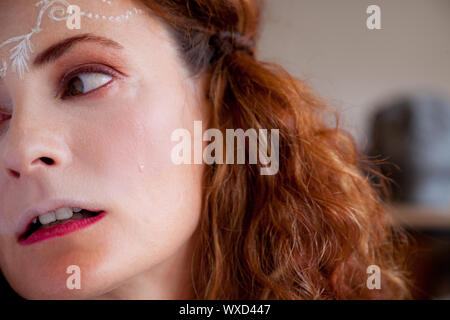 Portait of young sad woman crying with white henna tattoo on forehead, looking aside Stock Photo