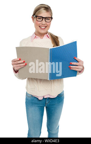 Bespectacled fashionable girl in sweater standing against white background and reading. Stock Photo