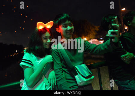 Young people gathering outside at night and making selfies during the celebration of the annual festival Loi Krathong in Chiang Mai, Chiang Mai Province, northern Thailand, Thailand, Southeast Asia, Asia. Stock Photo