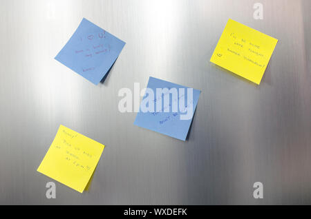 Reminder sticky notes with handwritten text hanging on a stainless fridge. Stock Photo