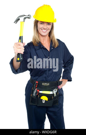 Construction worker in uniform holding up hammer with tool kit around her waist. Stock Photo