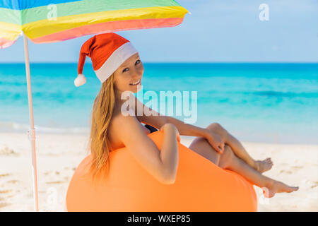 Woman on an inflatable beach couch and Christmas hat on the beach under an umbrella Stock Photo