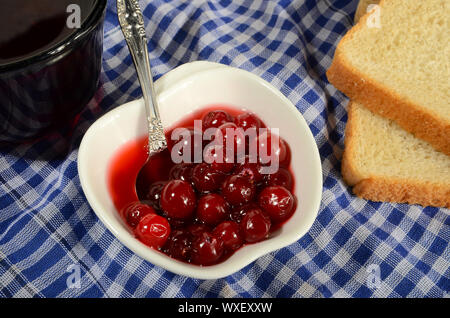 FRESH JAM FROM THE CRANBERRIES IN WHITE BOWL WITH SPOON TWO PIECES OF TOAST BREAD AND A MUG OF TEA Stock Photo