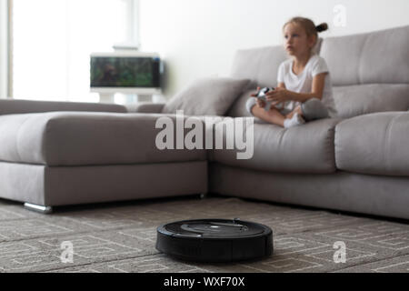 Robotic vacuum cleaning room while girl playing video game Stock Photo