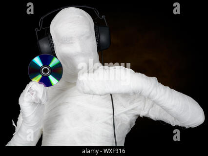 DJ in costume mummy with ear-phones and disc on black Stock Photo