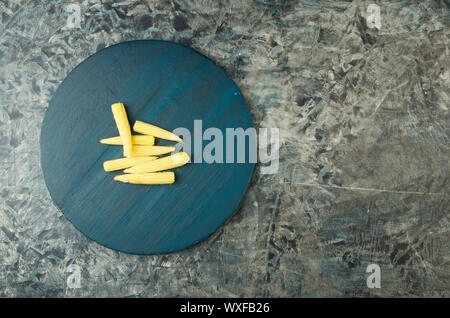 THE YOUNG CORN ON A ROUND WOODEN BOARD ON THE STONE SURFACE. Stock Photo