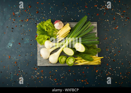 ONIONS GARLIC ON THE BOARD. GREEN ONIONS FEATHERS WITH THE HEADS OF GARLIC LYING ON A WOODEN BOARD ON A TEXTURED BACKGROUND. Stock Photo