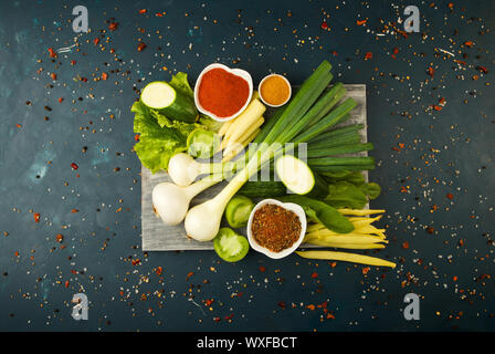 VEGETABLES ON WOODEN BOARD ON A STONE BACKGROUND. YOUNG HERBS ONIONS GARLIC GREEN BEANS YELLOW CORN ZUCCHINI BRIGHT SPICES LIE O Stock Photo