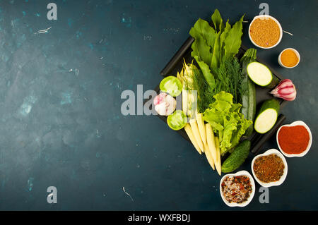 THE VEGETABLES IN THE BOX ON THE STONE A DARK BACKGROUND. YOUNG GREENS ONION GARLIC ZUCCHINI BRIGHT SPICES LAY IN A WOODEN TRAY Stock Photo