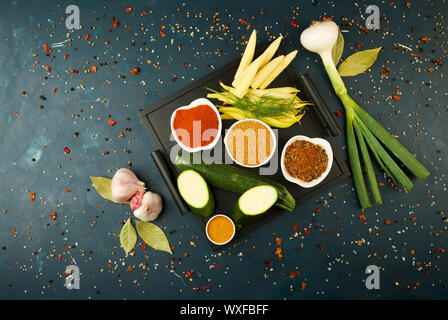 THE VEGETABLES IN THE BOX ON THE STONE A DARK BACKGROUND. YOUNG GREENS ONION GARLIC ZUCCHINI BRIGHT SPICES LAY IN A WOODEN TRAY Stock Photo