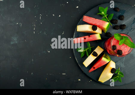 MELON WATERMELON BLACKBERRIES MINT AND A GLASS OF JUICE ON ROUND WOODEN BACKGROUND. RIPE WATERMELON JUICY MELON BLACKBERRY MINT Stock Photo